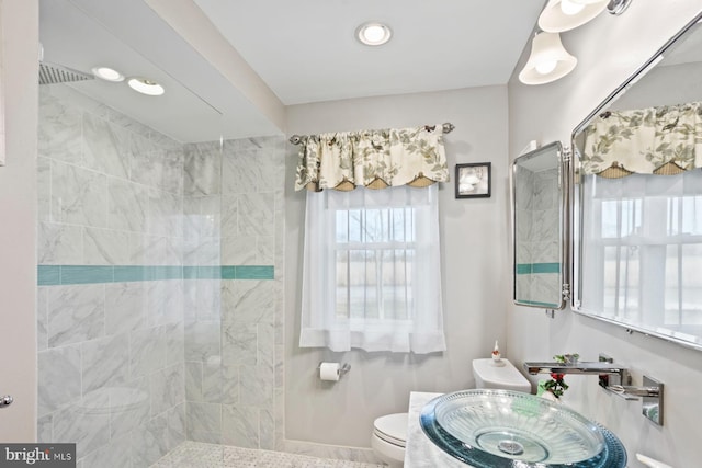 bathroom featuring a tile shower, toilet, and sink