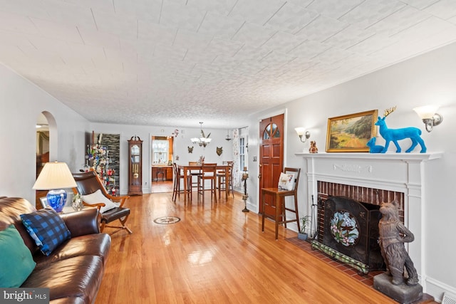 living room featuring wood-type flooring, a textured ceiling, and a brick fireplace