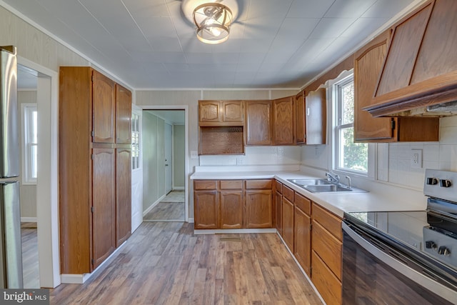 kitchen with a sink, stainless steel appliances, premium range hood, light wood finished floors, and brown cabinetry