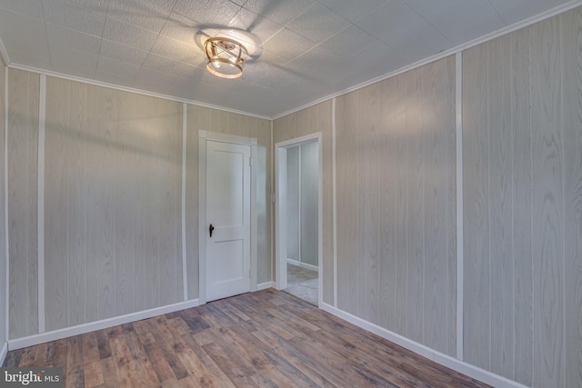 spare room with baseboards, wood walls, wood finished floors, and crown molding
