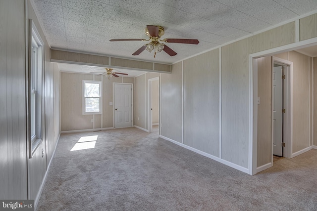 carpeted empty room featuring wooden walls and ceiling fan