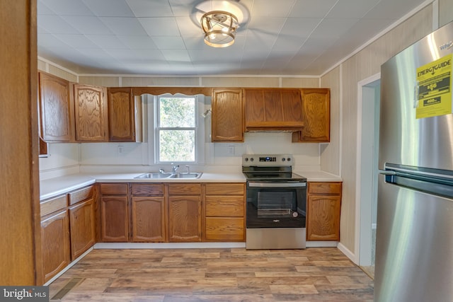 kitchen with light wood finished floors, brown cabinets, a sink, light countertops, and appliances with stainless steel finishes