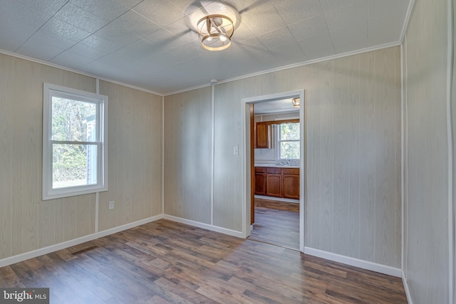 empty room featuring dark wood-type flooring, baseboards, and crown molding