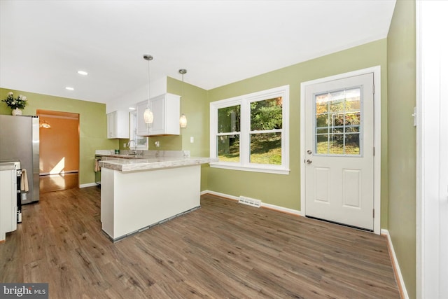 kitchen featuring dark hardwood / wood-style flooring, kitchen peninsula, white cabinetry, decorative light fixtures, and stainless steel refrigerator