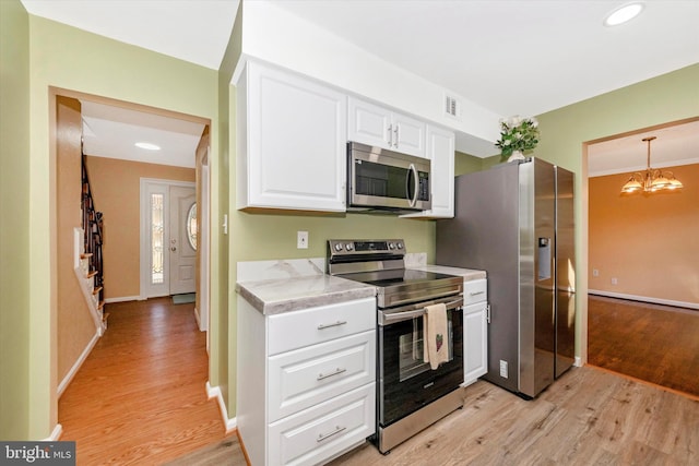 kitchen with white cabinets, appliances with stainless steel finishes, an inviting chandelier, light hardwood / wood-style floors, and decorative light fixtures