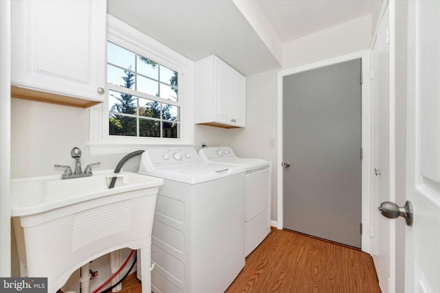 clothes washing area with sink, light hardwood / wood-style flooring, washer and clothes dryer, and cabinets