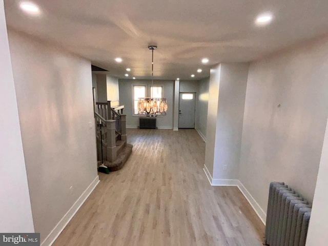 hallway with radiator, an inviting chandelier, and light hardwood / wood-style flooring