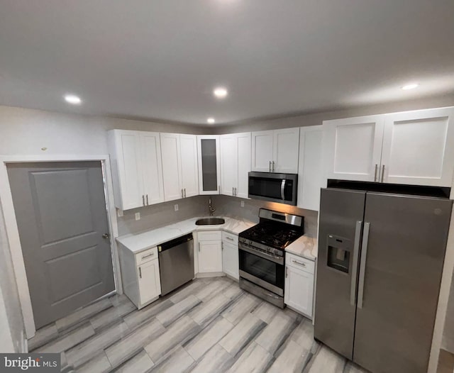 kitchen with stainless steel appliances, light hardwood / wood-style floors, white cabinets, and sink