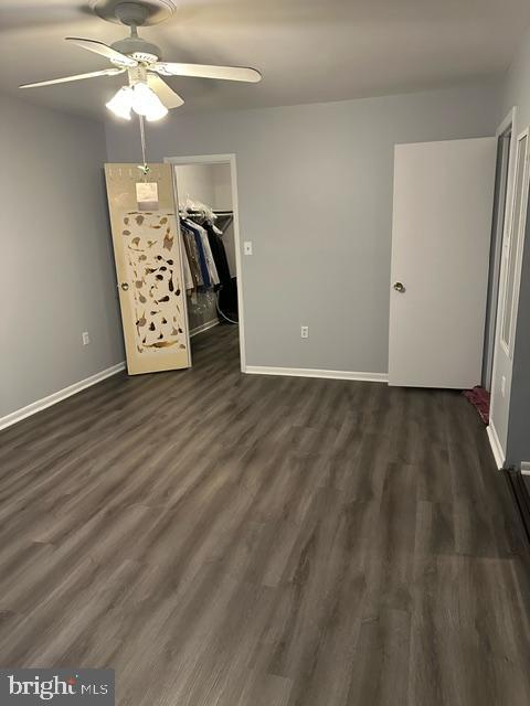 unfurnished bedroom featuring a closet, a spacious closet, ceiling fan, and dark hardwood / wood-style flooring