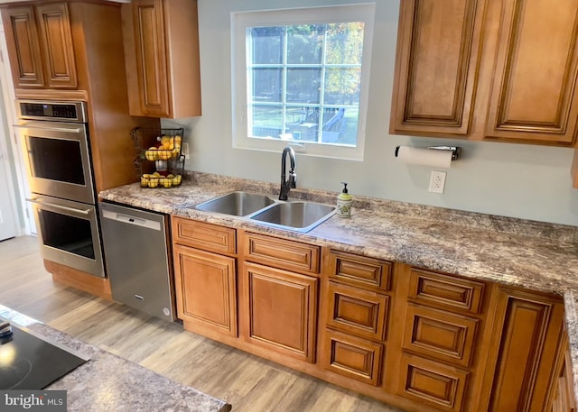 kitchen featuring sink, appliances with stainless steel finishes, light stone counters, and light wood-type flooring