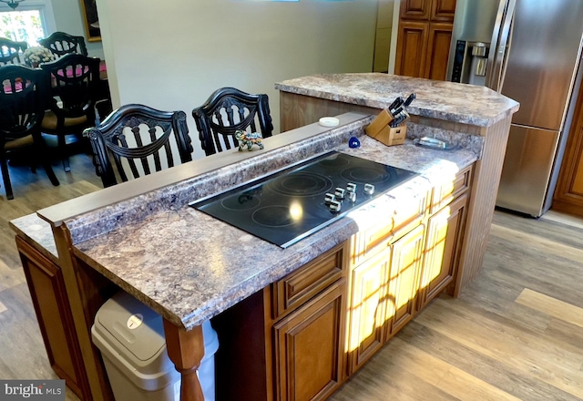 kitchen with light hardwood / wood-style flooring, a center island, black electric cooktop, and stainless steel refrigerator with ice dispenser