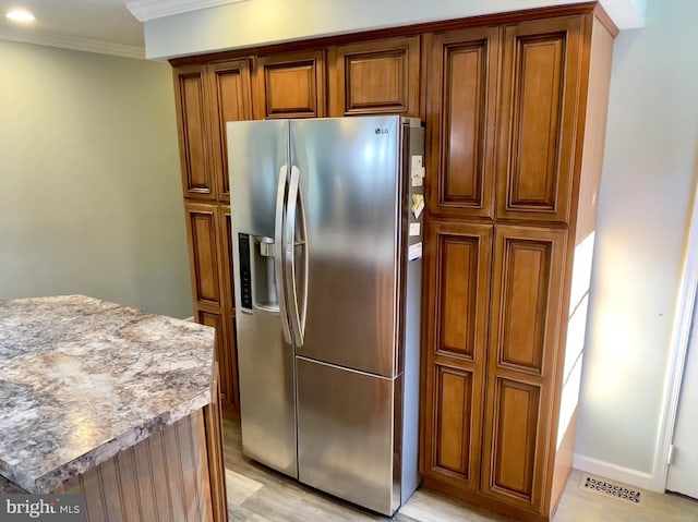 kitchen featuring ornamental molding, light stone countertops, stainless steel refrigerator with ice dispenser, and light hardwood / wood-style floors