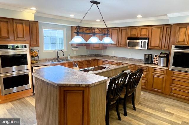 kitchen featuring sink, a center island, stainless steel appliances, decorative light fixtures, and light hardwood / wood-style flooring