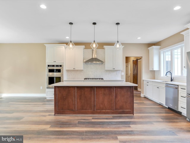 kitchen featuring appliances with stainless steel finishes, a barn door, a kitchen island, and wall chimney range hood