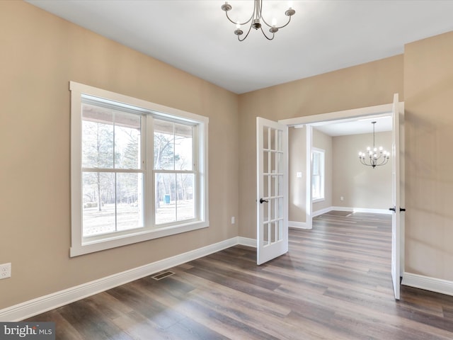 spare room featuring french doors, dark wood-type flooring, and an inviting chandelier