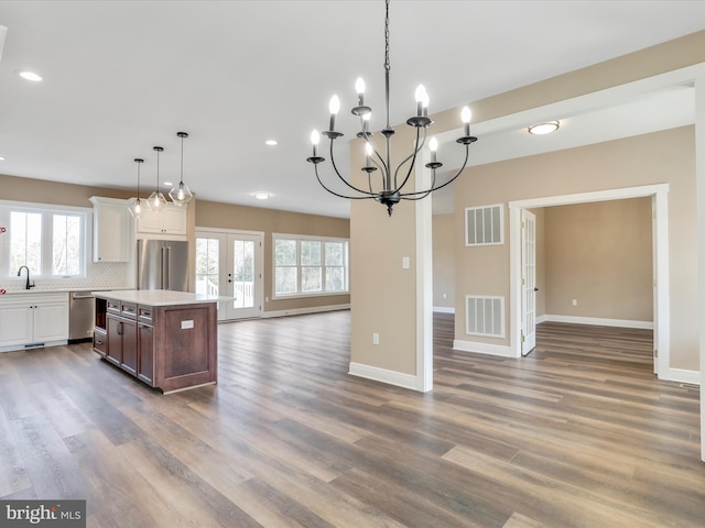 kitchen with a kitchen island, pendant lighting, decorative backsplash, white cabinets, and appliances with stainless steel finishes