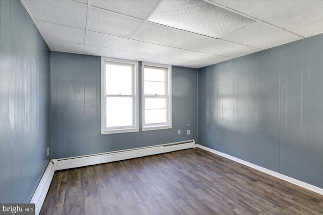 spare room with a baseboard radiator, a drop ceiling, and dark hardwood / wood-style flooring