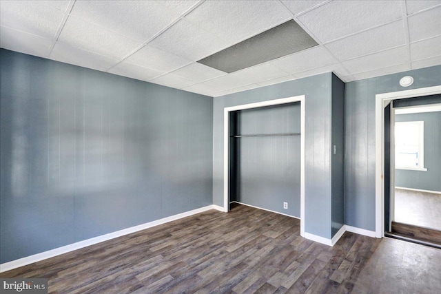 unfurnished bedroom featuring a drop ceiling, a closet, and dark hardwood / wood-style flooring