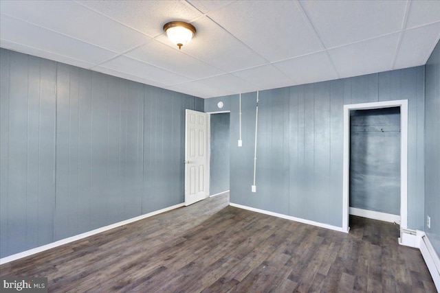 unfurnished room featuring wood walls, a drop ceiling, baseboard heating, and dark hardwood / wood-style floors