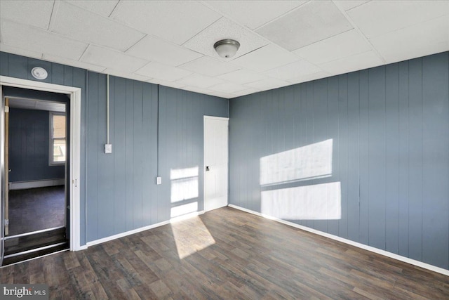 empty room with baseboard heating, wooden walls, and dark hardwood / wood-style floors