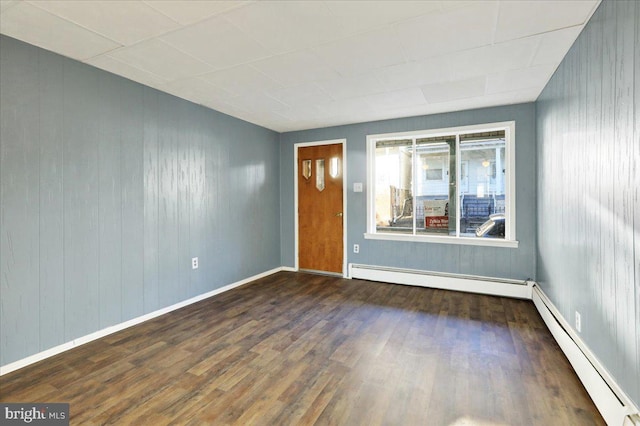 spare room with baseboard heating, dark wood-type flooring, and wood walls