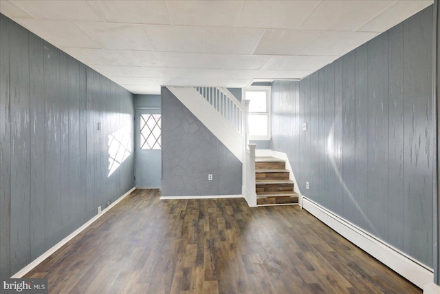 basement with wood walls, dark hardwood / wood-style floors, and a baseboard heating unit