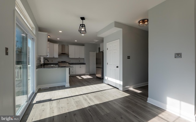 kitchen with appliances with stainless steel finishes, dark hardwood / wood-style flooring, wall chimney exhaust hood, pendant lighting, and white cabinets