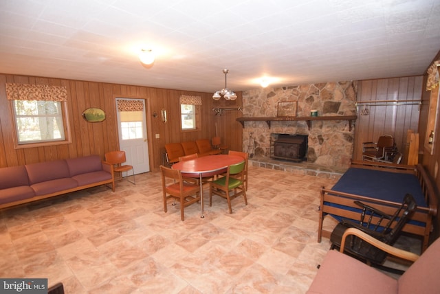 dining room with a notable chandelier, a stone fireplace, and wooden walls