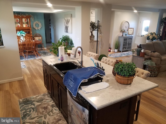 kitchen with dark brown cabinets, a kitchen island with sink, sink, light hardwood / wood-style flooring, and a breakfast bar area