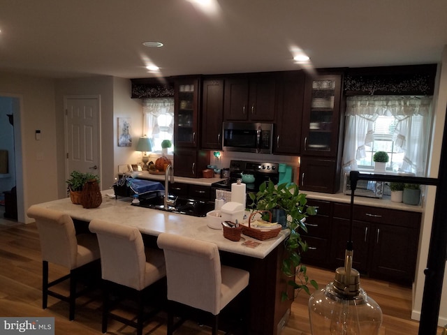 kitchen featuring sink, light hardwood / wood-style flooring, black range with electric stovetop, a breakfast bar area, and an island with sink