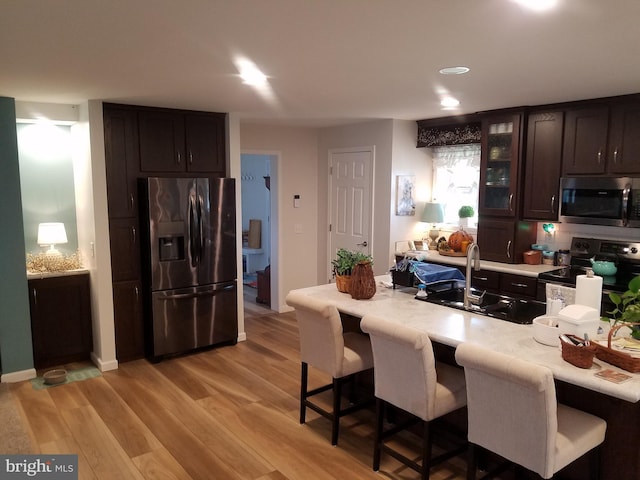 kitchen featuring dark brown cabinetry, sink, stainless steel appliances, a kitchen breakfast bar, and light hardwood / wood-style floors