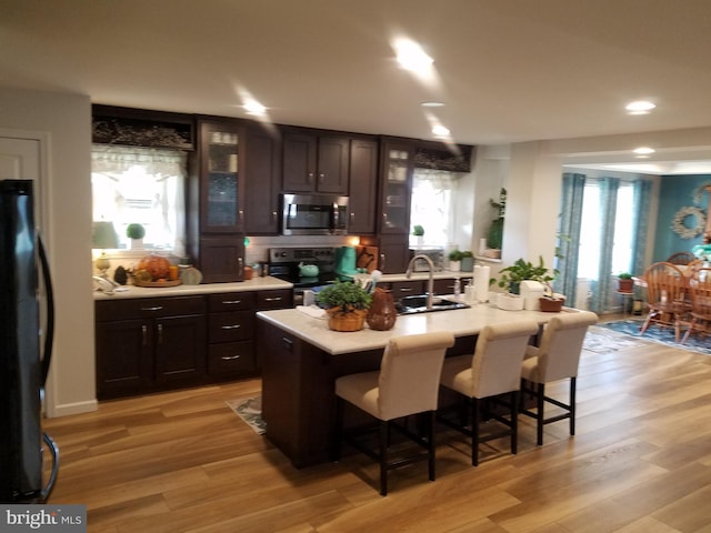 kitchen featuring a breakfast bar, an island with sink, light hardwood / wood-style flooring, and black appliances