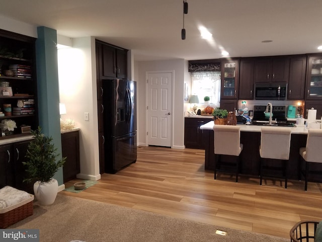 kitchen featuring black appliances, dark brown cabinets, light hardwood / wood-style floors, and a kitchen bar