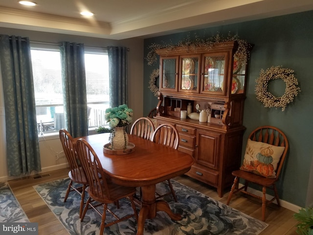 dining area with wood-type flooring, a raised ceiling, and ornamental molding