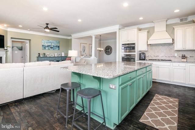 kitchen with a kitchen island, a kitchen breakfast bar, ornate columns, dark wood-type flooring, and premium range hood