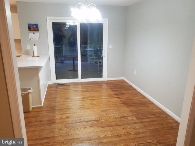 unfurnished dining area featuring wood-type flooring and an inviting chandelier