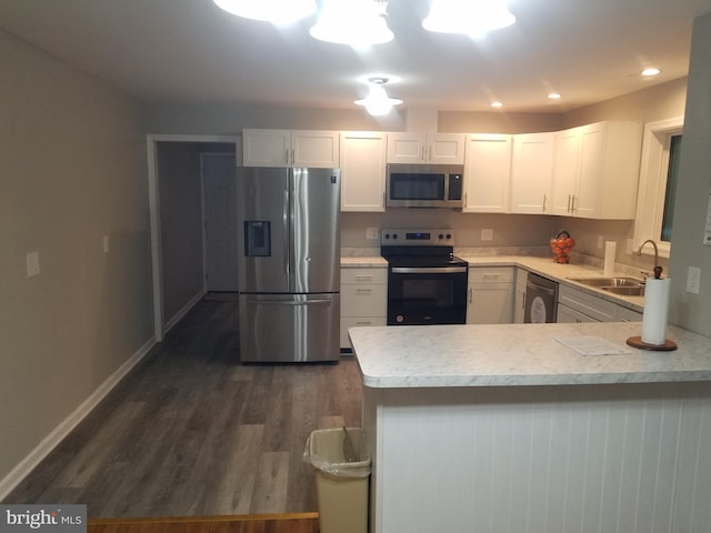 kitchen with kitchen peninsula, appliances with stainless steel finishes, dark wood-type flooring, sink, and white cabinetry