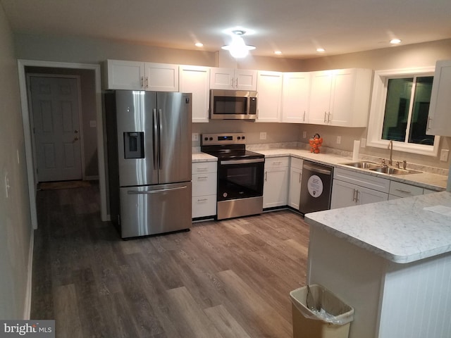 kitchen with kitchen peninsula, stainless steel appliances, sink, white cabinets, and hardwood / wood-style floors