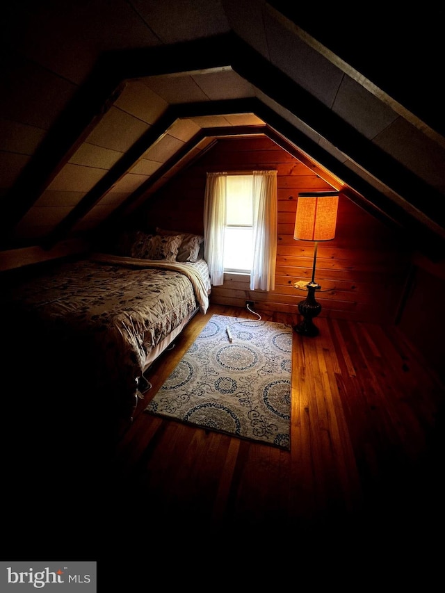 bedroom featuring lofted ceiling, wood walls, and hardwood / wood-style flooring