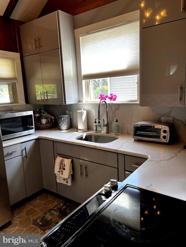 kitchen with sink, light stone counters, tasteful backsplash, and a wealth of natural light