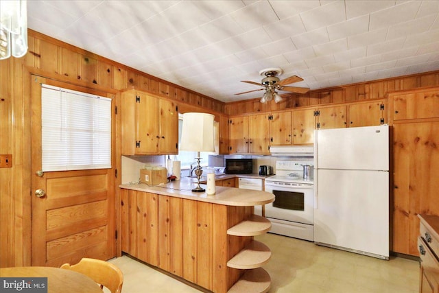 kitchen with kitchen peninsula, ceiling fan, wooden walls, decorative light fixtures, and white appliances