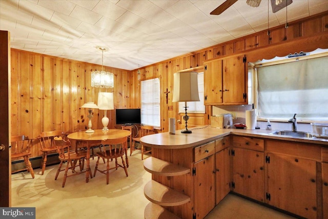 kitchen featuring kitchen peninsula, wood walls, decorative light fixtures, and sink