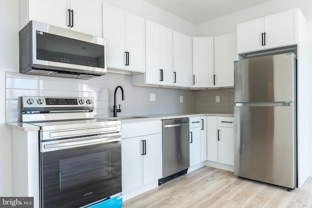 kitchen featuring white cabinetry, stainless steel appliances, light hardwood / wood-style floors, sink, and tasteful backsplash