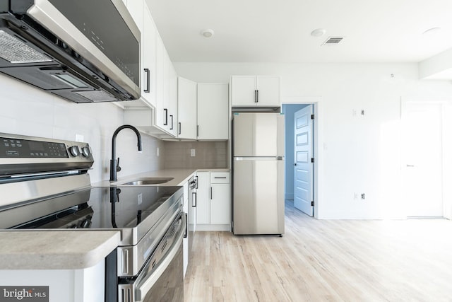 kitchen with appliances with stainless steel finishes, light hardwood / wood-style flooring, white cabinets, backsplash, and sink