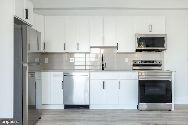 kitchen with appliances with stainless steel finishes, light wood-type flooring, white cabinets, decorative backsplash, and sink