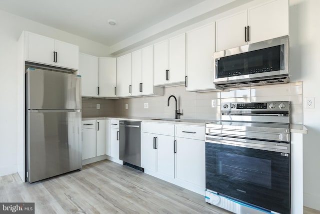 kitchen with appliances with stainless steel finishes, tasteful backsplash, white cabinets, and light hardwood / wood-style floors