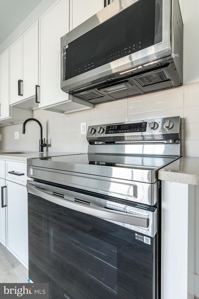 kitchen with sink, backsplash, appliances with stainless steel finishes, and white cabinets