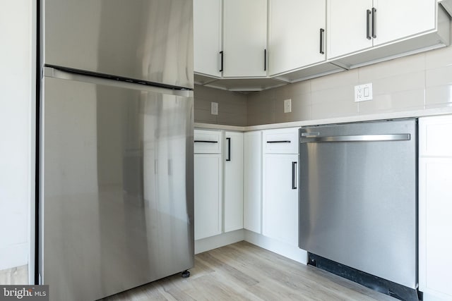 kitchen featuring light wood-type flooring, backsplash, appliances with stainless steel finishes, and white cabinets