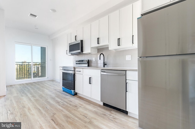 kitchen featuring appliances with stainless steel finishes, sink, light hardwood / wood-style floors, white cabinets, and tasteful backsplash