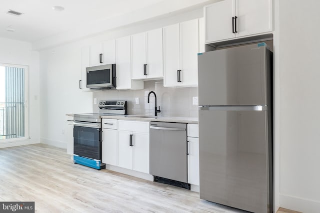 kitchen featuring stainless steel appliances, light hardwood / wood-style floors, backsplash, sink, and white cabinetry